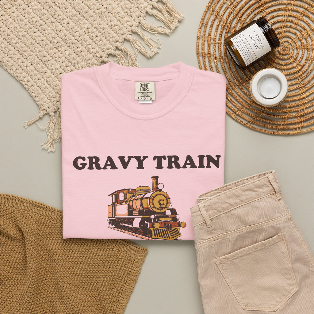 Gravy Train Conductor tee in Blossom pink, folded in a styled flat lay with a woven mat, candle and khaki shorts — locomotive print on the front