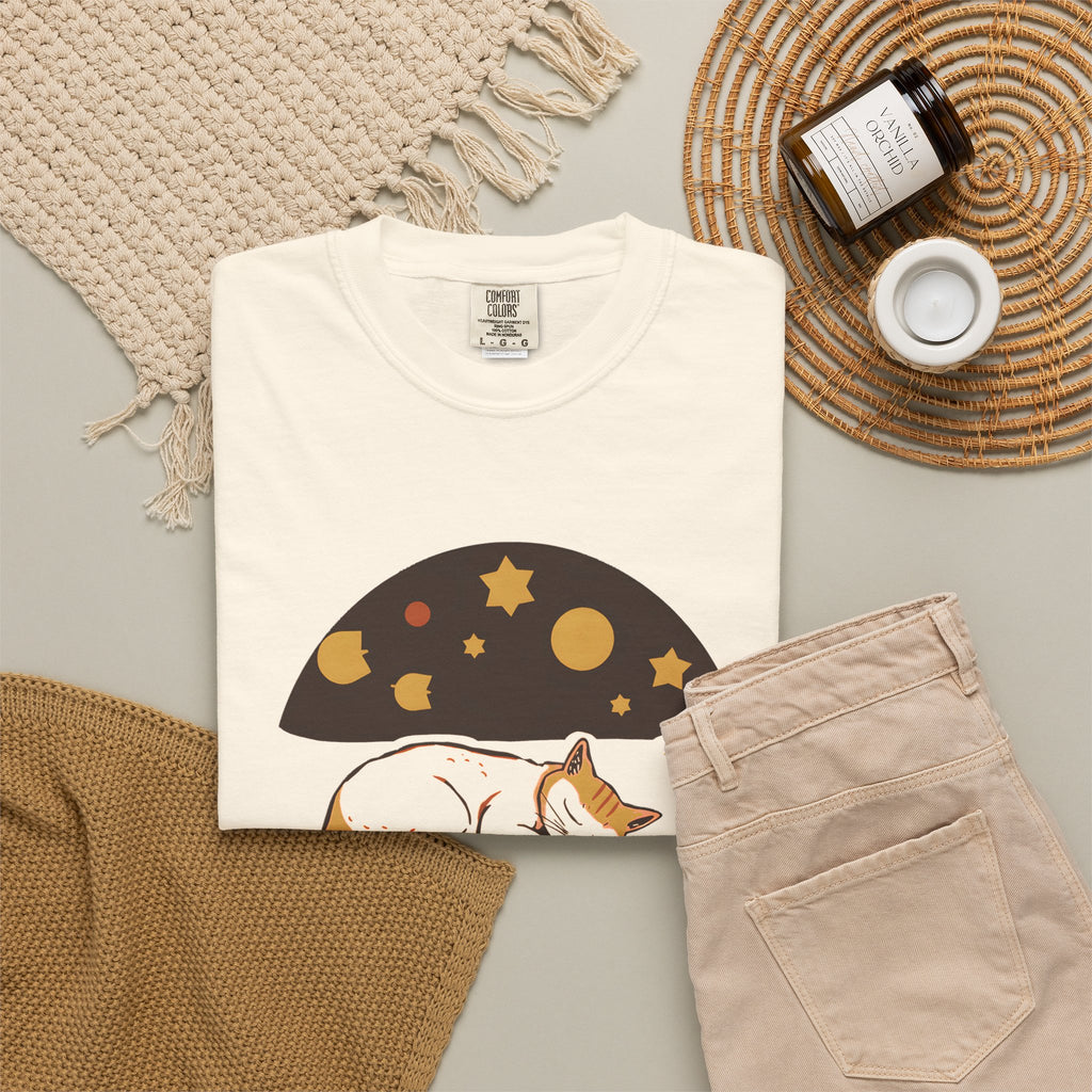 Lunch Break Read tee in Ivory, folded in a styled flat lay with a woven mat, candle and khaki shorts — sleeping cat print on the front